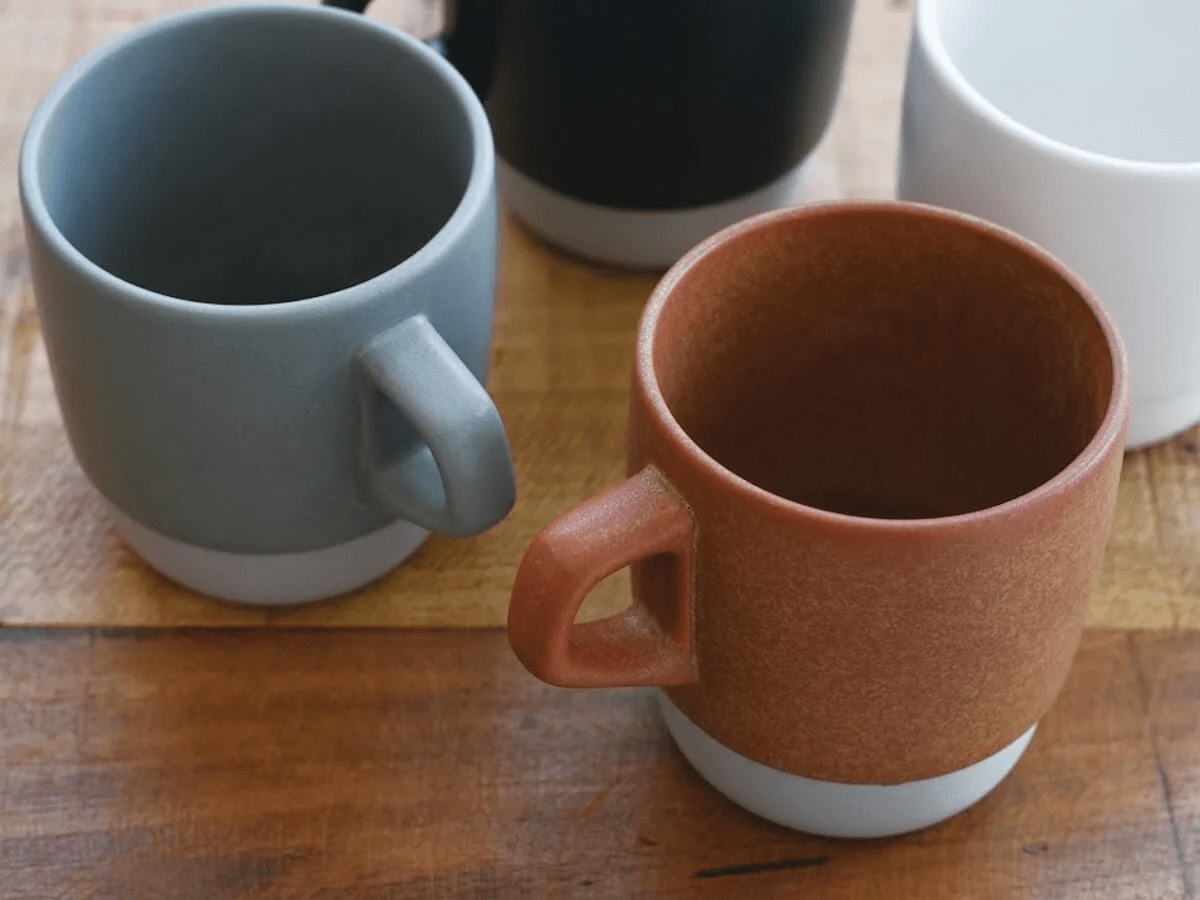 Four Kinto mugs in different colors on wooden surface